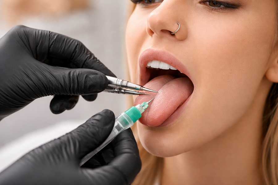 Piercing języka wykonywany przez specjalistę – moment przekłuwania języka sterylnym wenflonem w profesjonalnym gabinecie piercingu.