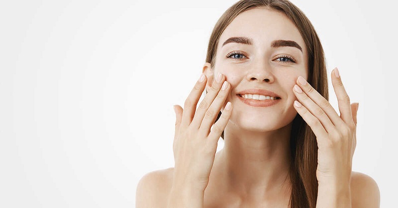 uśmiechnięta brunetka z długimi włosami dotykająca palcami policzków pokazuje wypielęgnowana twarz